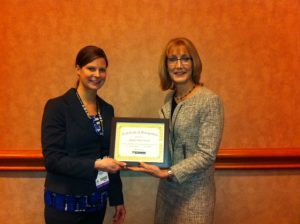 MIA's Sarah Gregg presents a certificate to Diane Hayden, AKDO's showroom supervisor. AKDO was named MIA's CEU Educator of the Year for 2014.