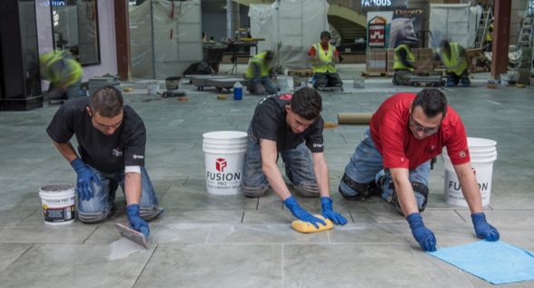With a teamwork grouting method, one installer spreads grout across the joints, one shapes the joints with a sponge and one cleans the tile with a microfiber towel.